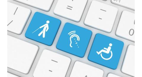 电脑键盘的近景. 三个键是浅蓝色的. 一个是一个坐在轮椅上的人的象征. 一种是辅助性倾听的符号. 一个是一个人拄着拐杖走路的象征.