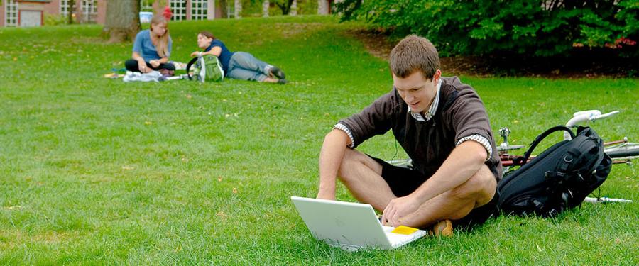 student sitting on lawn working on laptop