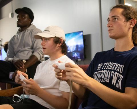 Three students sitting on couch playing video games