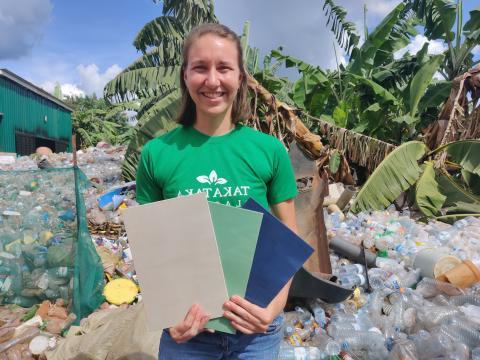 Paige outside standing in front of piles of plastic, holding a recycled plastic product