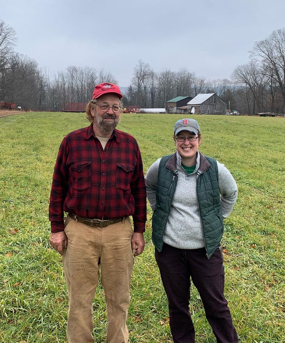 A photo of a white woman and an older white man standing in a farm field.