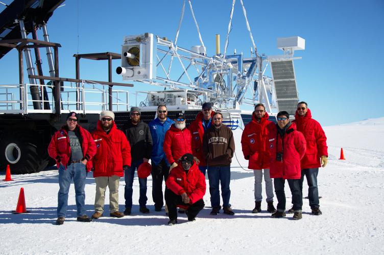 Team of researchers in Antarctica stand in front of a large telescope.
